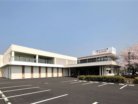 白い2階建ての建物はエル字型で広い駐車場があり、2階部分にはベランダもある。