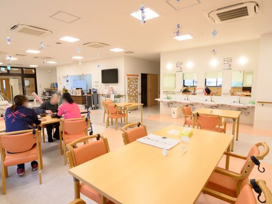 大きなテーブルがゆったりと配置されている食堂である。洗面スペースが設けられている。入居者様とスタッフがテーブルを囲んでいる。