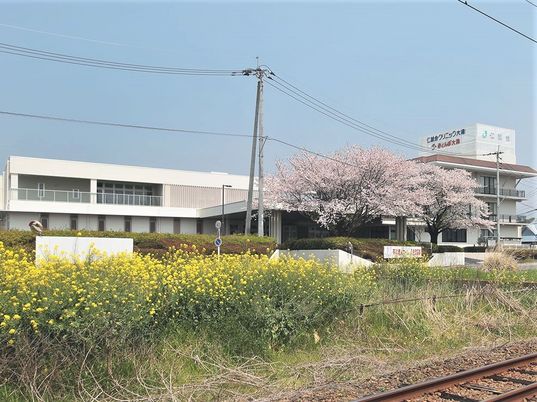 白い建物の周りに花の花や桜の花が咲き、すぐそばに線路もある。
