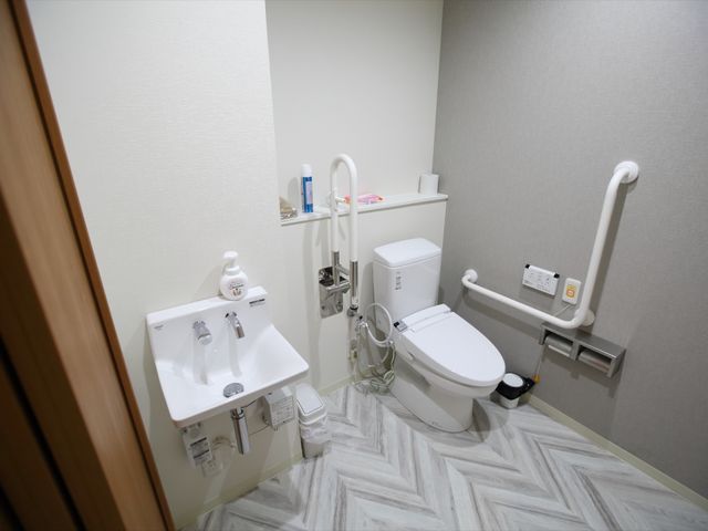 バリアフリーなトイレ設備 トイレ 手すりが付いた清潔感のあるトイレです。床と壁の色が落ち着いており、利用者の快適な日常生活を支援します。
