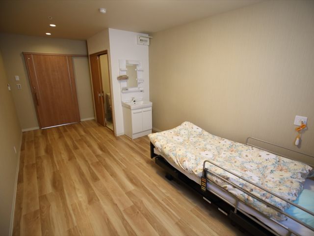 居室の広々とした空間 居室 木目調の床が温かみを感じさせる個室で、安心して過ごせる環境が整っています。ベッドや洗面設備が備わり、快適な日常生活が送れます。