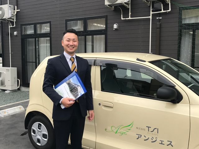 スタッフと車の前立つ 笑顔のスタッフが出勤準備をしており、清潔感ある服装とアクセサリーがプロ意識を反映しています。