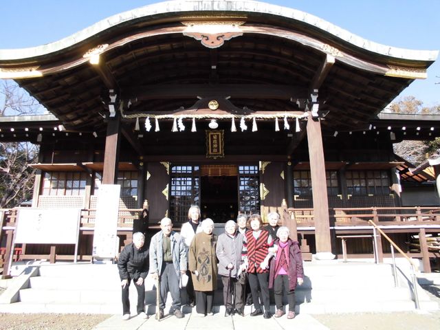 神社の前にいる人々 暖かい日差しの中、神社の前で笑顔を見せるスタッフと利用者様の姿。共に過ごす時間の豊かさが感じられます。