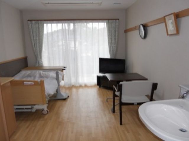 ベッドと洗面台の居室 居室 広々とした居室には自然光が差し込み、明るい雰囲気です。快適に過ごせる設備が整っています。