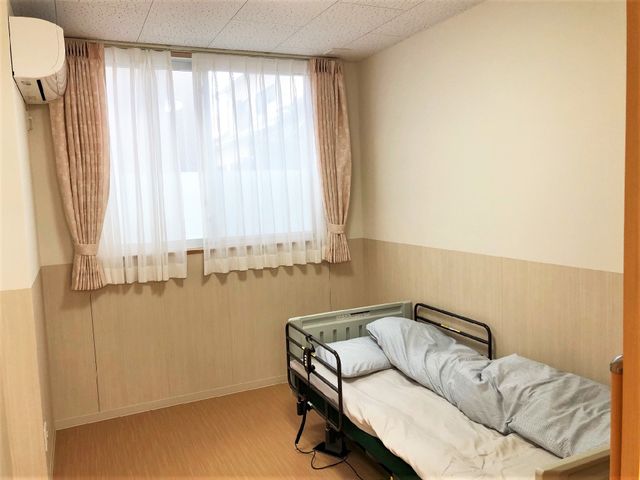 居室のベッドと窓 居室 シンプルなデザインの居室には、必要な設備が整っており、日当たりも良好です。個々の生活スペースを大切にできる環境が整っています。