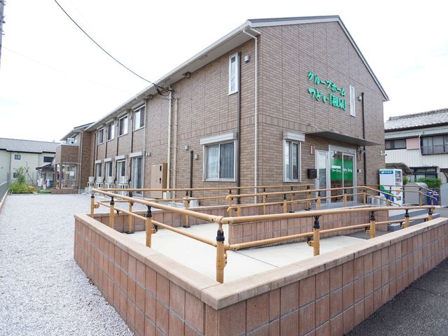 茶色の建物エントランス 外観 バリアフリー設計のエントランスが印象的です。入口のスロープは、安全に出入りするための手すりが整っており、皆様の快適な日常をサポートします。
