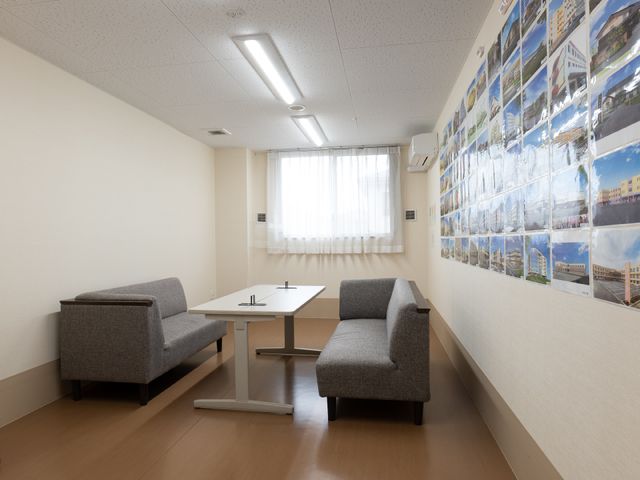 シンプルな休憩室 相談室 落ち着いた色合いのソファが配置され、ゆったりと休憩できる空間です。壁には地域の写真が飾られ、開放的な雰囲気を演出しています。
