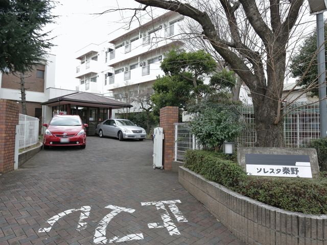建物前の車とエントランス 施設入口 広々とした入り口があり、来訪者を温かく迎えます。立地も良く、通勤に便利な環境です。