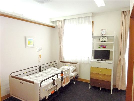 施設の写真 介護用ベッドが壁際に置かれた居室。日当たりがよく、テレビや収納家具も付いている。