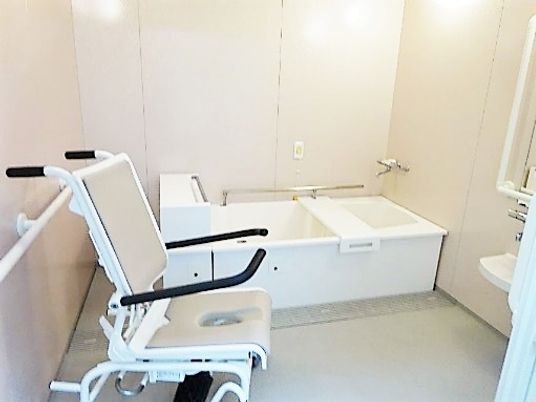 施設の写真 白い浴槽が置かれた広い浴室。シャワーや手すり、浴室用車いすも設置されている。