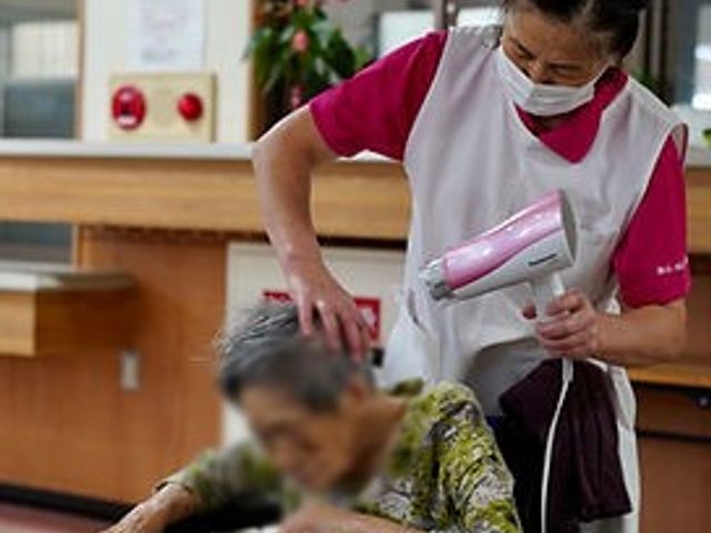 髪を乾かすシーン 美容室 明るい空間でヘアドライをしている様子です。介護職員が入居者の髪を優しくケアしています。