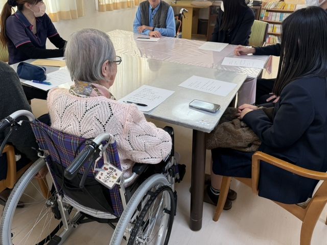会議中のテーブル 内観 車椅子の利用者とスタッフがテーブルを囲んで話し合う場面です。温かい空気感で活気ある交流が印象的です。