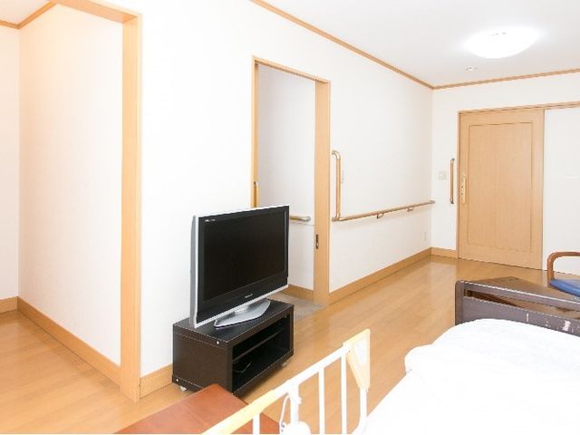 居室のテレビとベッド 居室 落ち着いた色調の居室です。壁に手すりが付いており、安全に配慮された設計となっています。