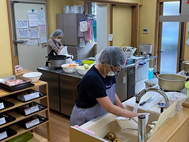 調理中のスタッフ二人 手際よく調理作業に勤しむスタッフの姿が見られます。清潔感のあるキッチンで、毎日の食事の準備が行われています。