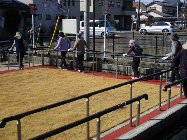 歩行訓練を行う人々 日差しが明るい屋外での歩行訓練風景です。支えのある手すりを使い、安全に体力向上を図っている様子がみられます。
