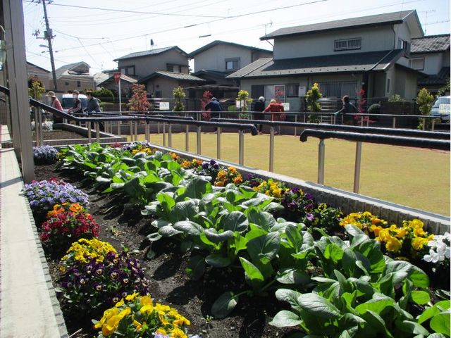 中庭の花壇と散歩中の人々 ゆったりとした中庭で、色とりどりの花壇を眺めながら散策を楽しむ様子が見受けられます。日々の暮らしに彩りを与える空間です。