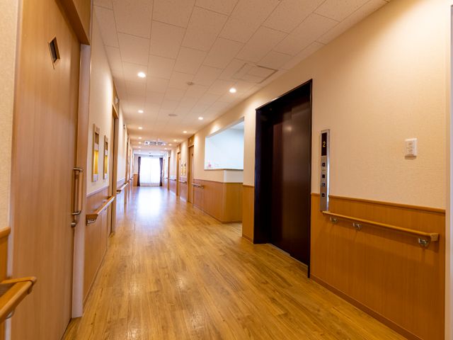明るく清潔な廊下 廊下 広々とした廊下は、木目調で温かみがあり、訪れる方々へのおもてなしの心を感じさせます。壁に掛けられたアートも空間に彩りを加えています。