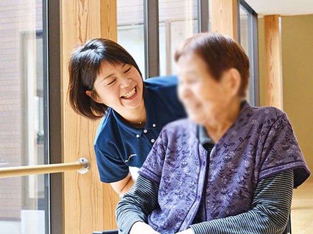 笑顔のスタッフと利用者の様子 内観 自然光が差し込む明るい空間で、スタッフが利用者と笑顔で交流しています。安心感のある雰囲気です。