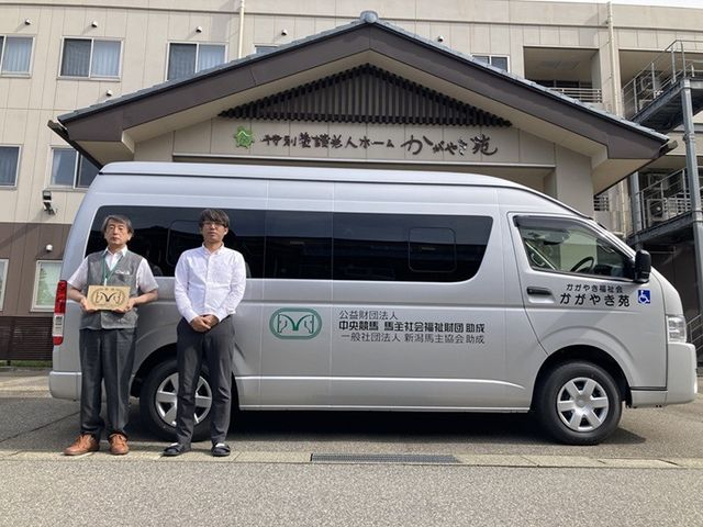 送迎車と建物外観 外観   送迎用の車両が建物前に停まっており、施設名の看板も見えます。職員の方が写っていて、働く場の雰囲気が伝わります。