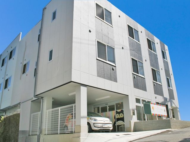 白い外観の建物 外観   白とグレーを基調にしたすっきりした建物です。1階に車寄せがあり、出入りのしやすさがうかがえます。