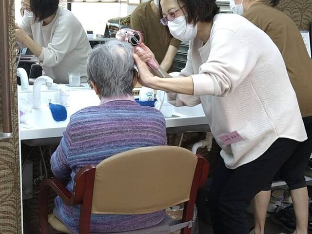 スタイリング中の理美容室 理美容室 鏡の前で、笑顔のスタッフが丁寧にヘアケアを行っています。温かい雰囲気の中で快適に過ごせます。