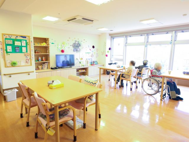 明るく広々とした休憩室 共有スペース 窓から自然光が差し込む温かな雰囲気の休憩室です。車椅子を利用される方々がリラックスしながら会話を楽しんでいます。