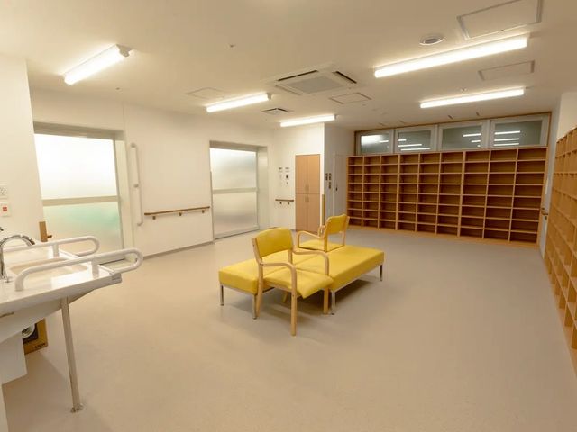 黄色の椅子がある休憩室 休憩室   明るく広めの休憩室です。中央に椅子が置かれ、手すりや収納棚も見えて、落ち着いて過ごしやすい印象です。