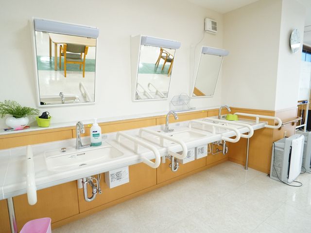 洗面台と大きなミラー 洗面台 手すり付きの洗面台が並び、安全に配慮された環境です。清潔感あふれるこのスペースで、毎日の身だしなみを整えられます。