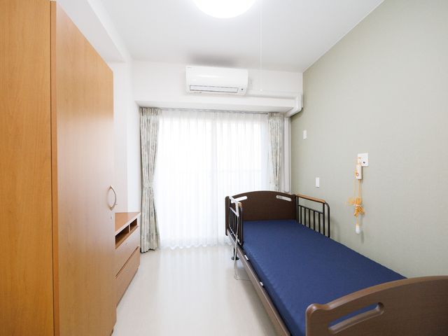 清潔感あるシンプルな居室 居室 窓から光が差し込む広々とした居室は、清潔感があり静かな時間をお過ごしいただけます。ベッドの横には必要な物をすぐ手に取れるよう棚が完備されています。