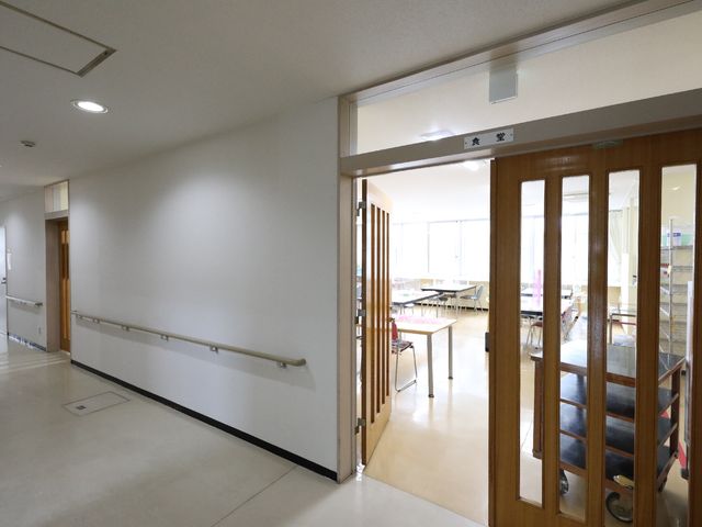 廊下から見た多目的室 廊下 明るい廊下の先には、ゆとりのある多目的室が確認できます。開放感のあるガラス戸が、利用者様のコミュニケーションの場を提供しています。