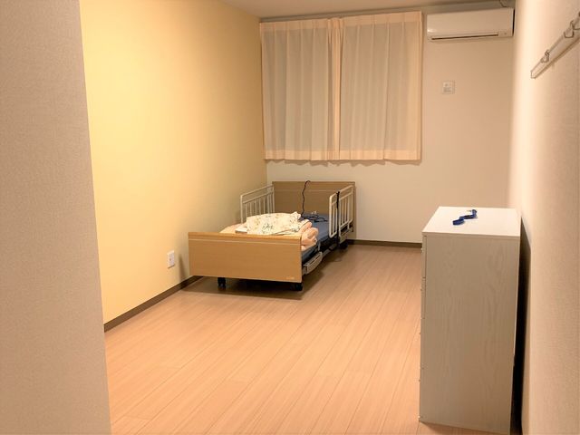 居心地の良い居室 居室Aタイプ ベッドとサイドキャビネットが置かれた快適な個室です。温かみのある色合いで落ち着いた雰囲気が演出されています。