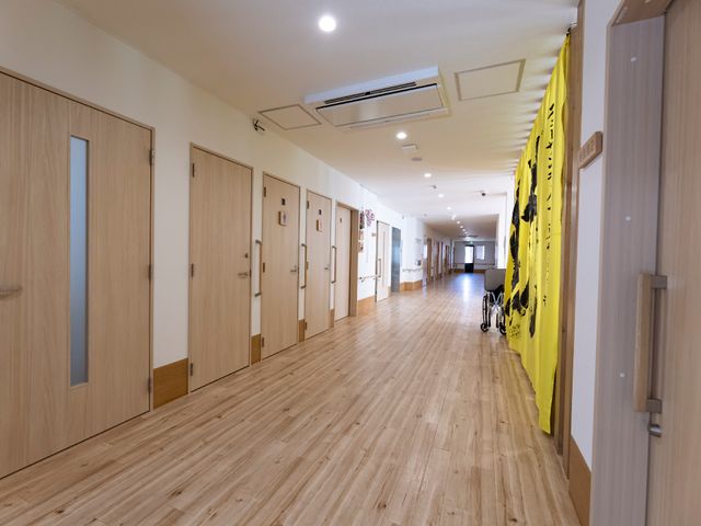 明るい廊下と部屋の扉 廊下 清潔感あふれる廊下は、ゆったりとした空間を確保し、車椅子の方も快適にお過ごしいただけます。壁にはアートが飾られ、心地よい環境が整っています。