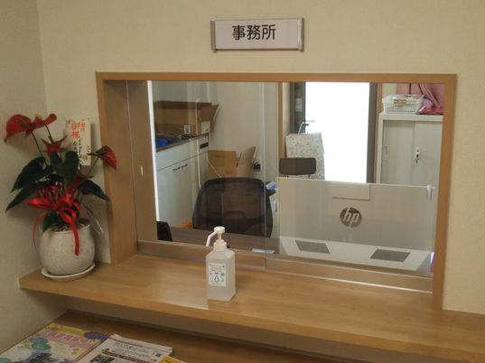 施設の写真 ガラス戸の前に消毒液や観葉植物、冊子などが並べられた受付