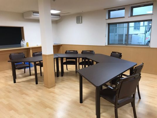 施設の写真 黒い椅子と机が半円を描くように並べられたフローリングの食堂