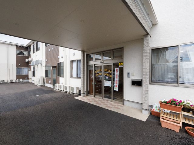 エントランスの明るい外観 外観 広々とした入り口は、訪れる方を温かく迎え入れる雰囲気があります。エントランス脇の緑や花は、来訪者に安らぎを提供します。