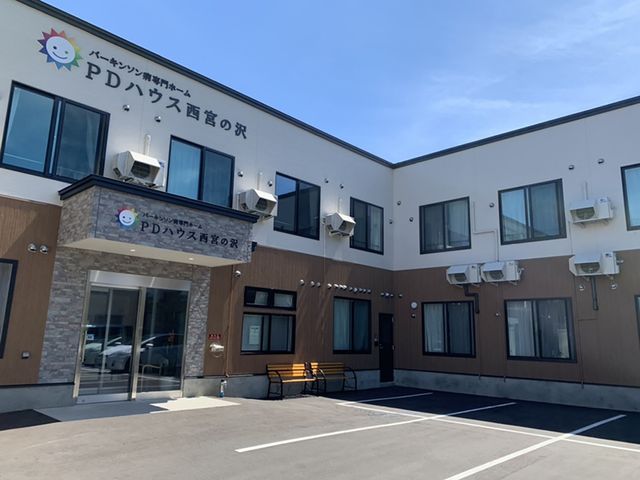 入り口のある建物外観 外観 広々とした駐車スペースを備えた施設のエントランスです。建物の周囲には豊かな自然が広がっています。