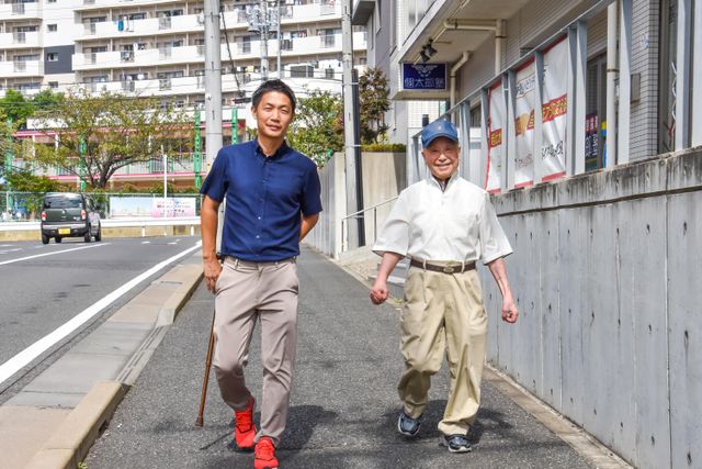 散歩する二人の人物 笑顔で一緒に歩くスタッフと利用者の姿が、心地よいコミュニケーションの場を物語っています。ここでは支え合いながら、日々の活動を楽しむ様子が窺えます。