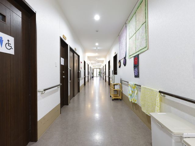 廊下の壁にアート飾る 廊下 手すり沿いの清潔な廊下は、アートワークで彩られ快適な空間を提供しています。廊下にはセンス良く配置された椅子も見受けられます。