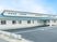 平屋建ての建物の外壁は白でグリーンの屋根が付いている。広い駐車場があり、日当たりのいい場所に建っている。