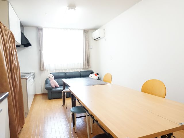居室のゆったり空間 共有スペース 広々とした居室には、快適なソファとダイニングテーブルが配置され、一人の方がリラックスしてお過ごしです。優しい日差しが差し込む窓辺で穏やかな時間をお過ごしいただける環境が整っています。