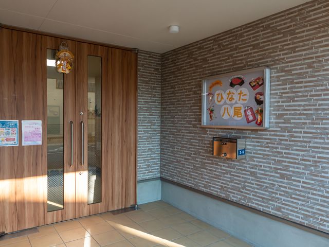 入り口と掲示板の風景 エントランス 温かみのある木目調の入口には、色鮮やかな掲示物が訪れる人を出迎えています。明るく開放感のあるこのエントランスが、新しい職場の第一印象になるかもしれません。