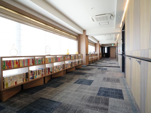 本棚付廊下の明るい空間 廊下 手すりに沿って明るく広い廊下が延びており、壁一面の本棚が心地よい静けさを提供しています。読書を愛する方には、特におすすめの職場環境です。
