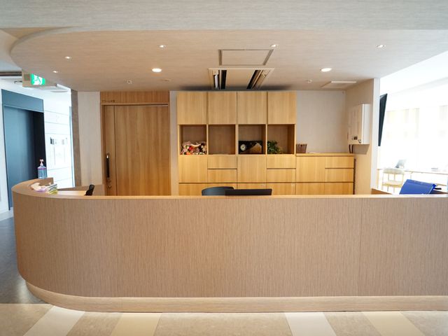 清潔感のあるフロント 受付 温かみのある木目と明るい照明が特徴の受付エリアです。患者さまの応対に真摯にあたるスタッフの姿が印象的です。