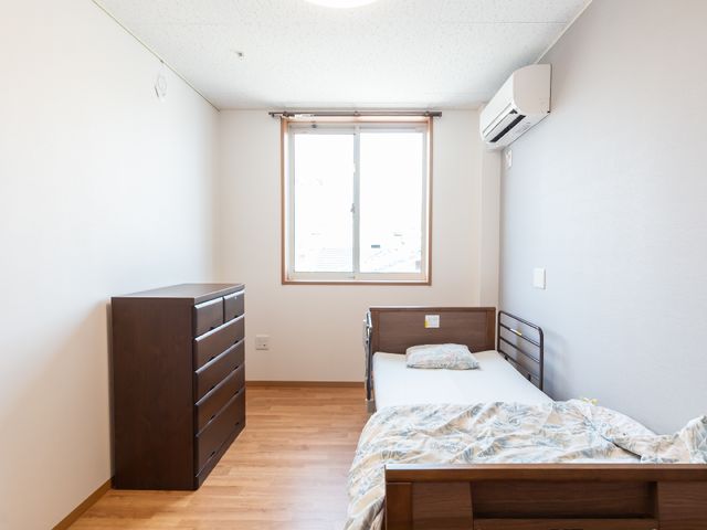 清潔感のある居室 居室 余裕のあるスペースに配置された家具とベッドが心地よさを感じさせます。日当たりの良い窓からは落ち着いた外の景色を眺めることができます。