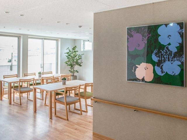 明るい居室の一角 リビングダイニング 採光に優れた居室で、木目調のテーブルとイスが配置され、落ち着いた雰囲気を醸し出しています。壁にはアートが飾られ、安らげる空間が提供されています。