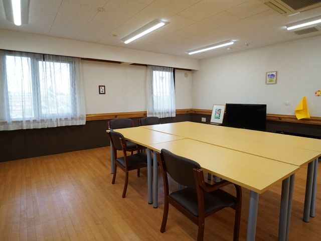 椅子とテーブルのある部屋 談話コーナー 広々とした空間の多目的室があり、静かで落ち着いた雰囲気で様々な活動が行えます。明るく開放的な窓辺は、心地良い自然光を取り込んでいます。