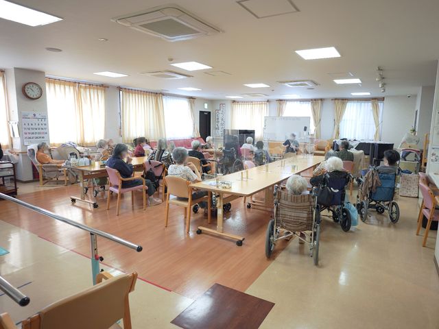 利用者憩いの食堂風景 共有スペース 日差しの優しい光が差し込む食堂で、利用者の方々がそれぞれの時間を過ごしています。様々な活動が行われる広く開放的な空間があります。