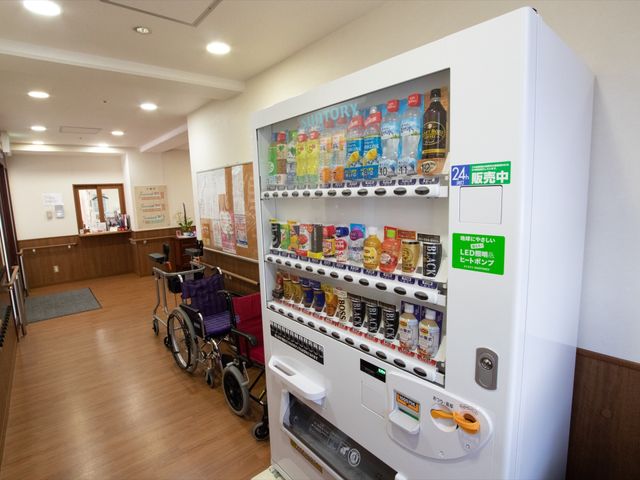 自動販売機と車椅子 廊下 ロビーに設置された自動販売機では、好きなドリンクを手軽に選べます。待合の時間も快適に過ごせる工夫があります。