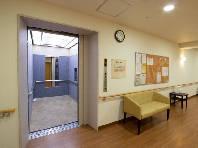 清潔感あるエレベーターホール エレベーター 手すりが設けられたエレベーターホールは、利用者の移動を支える配慮が感じられます。周囲には広々とした休憩スペースも備わっています。