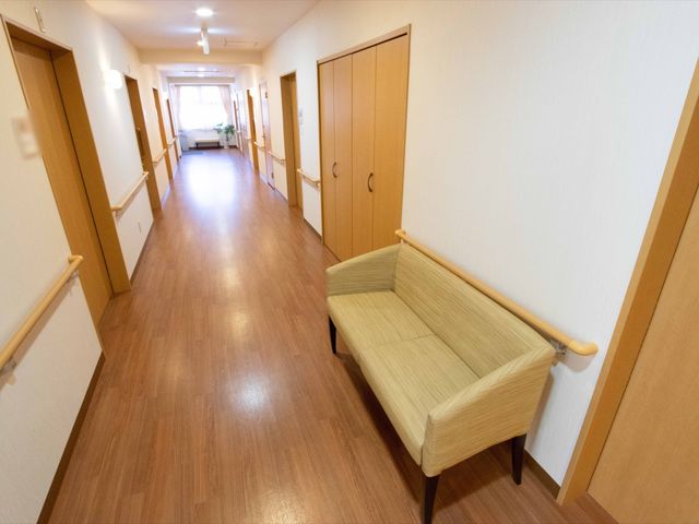 明るく広い廊下 廊下 手すりが設置された温かみのある廊下は、利用者が安心して歩行できる環境を提供しています。ベンチも設置され、休憩しながらの移動も快適です。